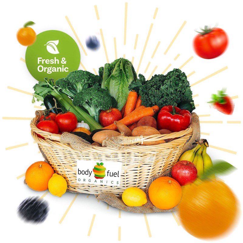 Body Fuel Organics signature produce bin — basket overflowing with leafy greens, broccoli, tomatoes, sweet potatoes, lemons, oranges, apples and bananas, with a Fresh & Organic badge